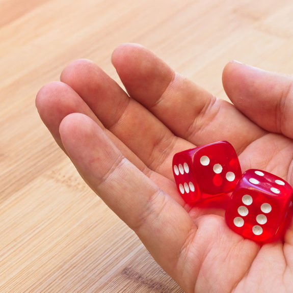 person-holding-two-red-dice-wooden-surface